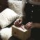 woman in grey sweater and blue denim dungarees sitting on brown and white sofa opening a yellow gift box closeup photography